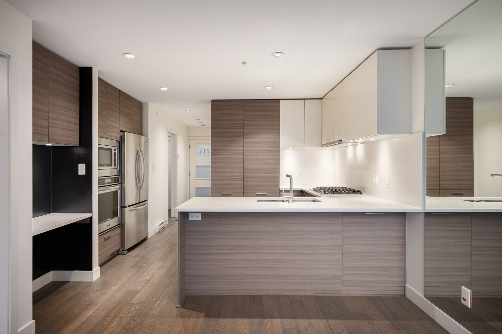 Modern kitchen with wood cabinets, white countertops, built-in stainless steel appliances, gas stove, and dark wood flooring.