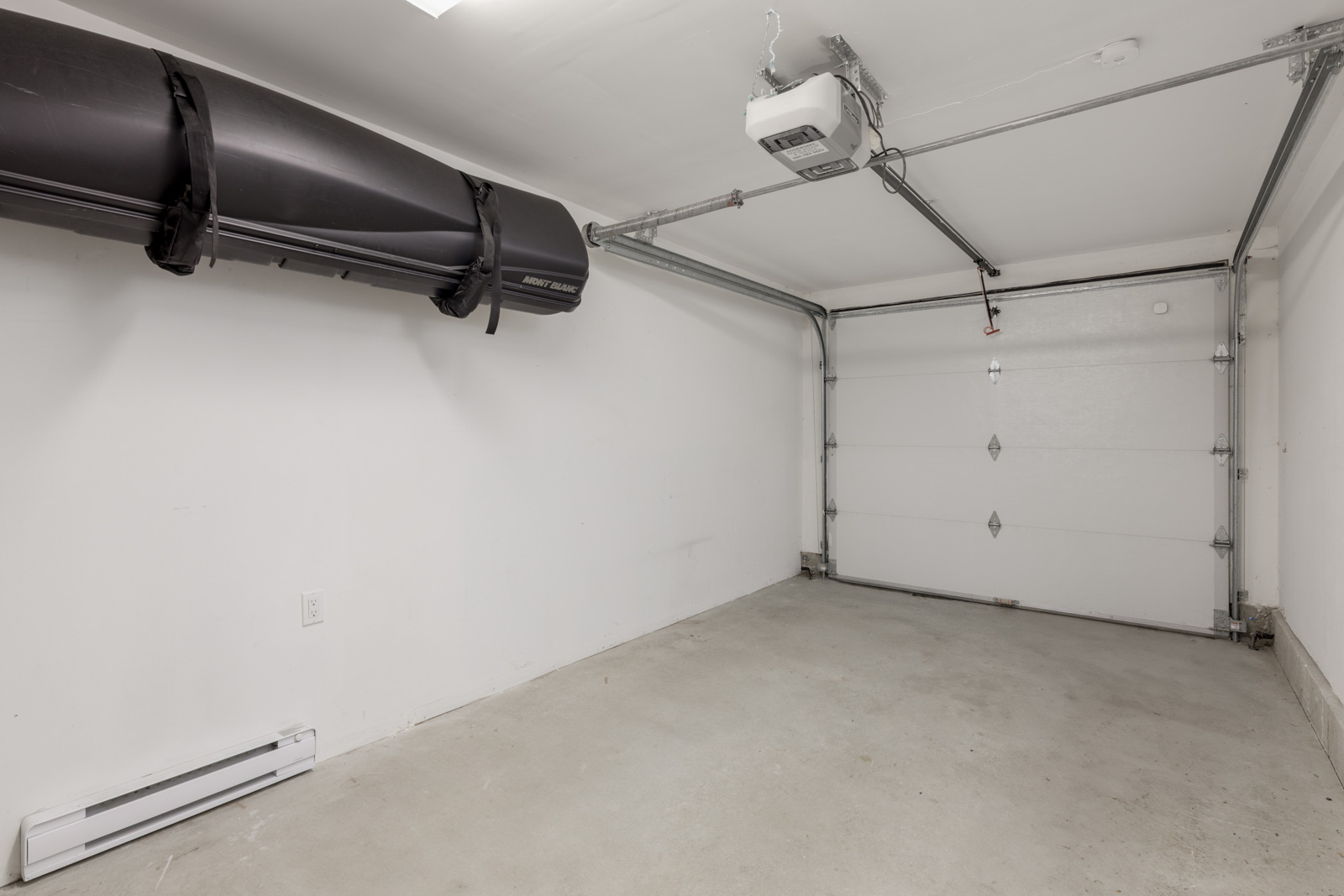 Empty single-car garage with white walls, closed overhead door, ceiling-mounted storage rack, and concrete floor.