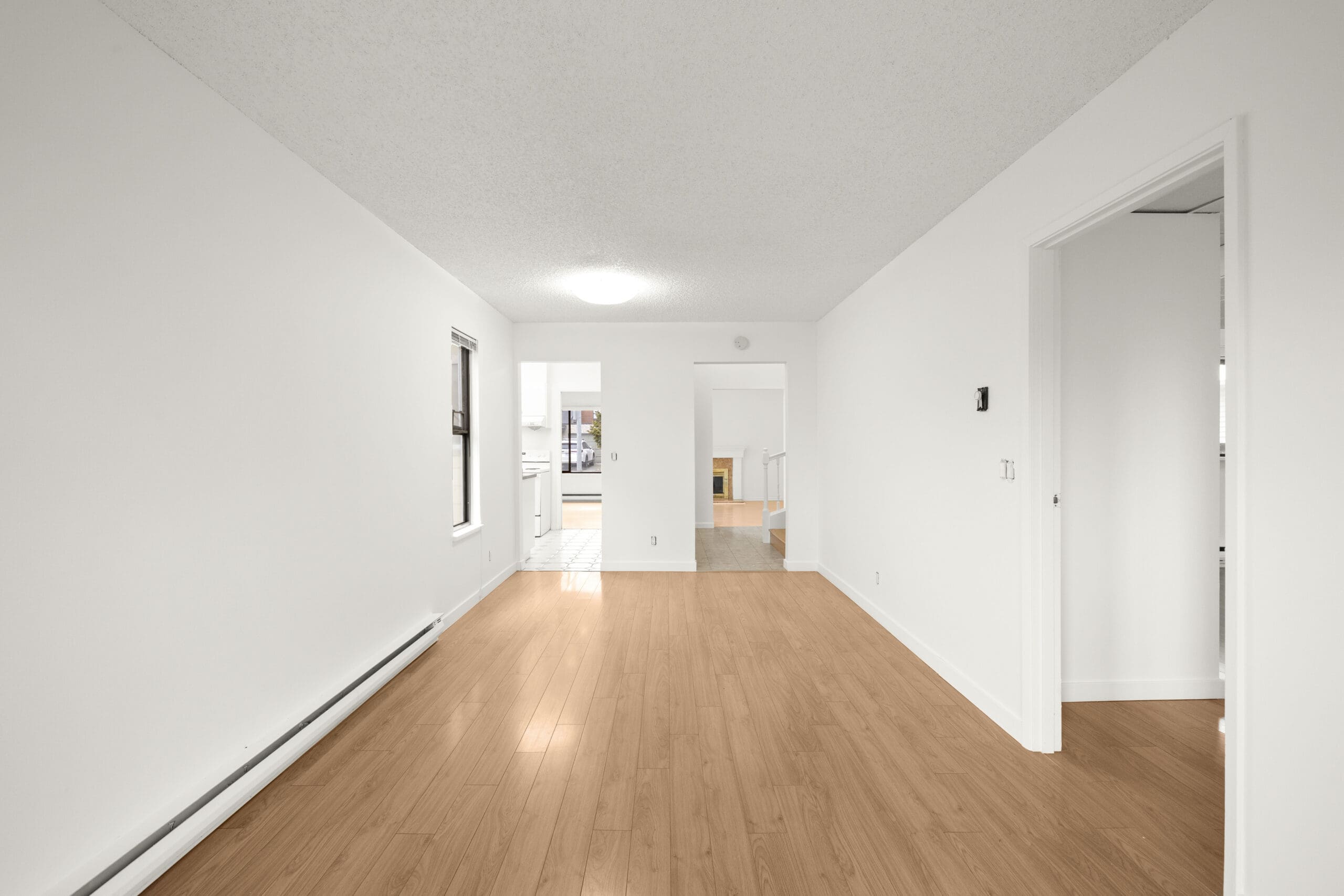 Unfurnished room with white walls, wood flooring, a window, and two doorways leading to other areas of the home.