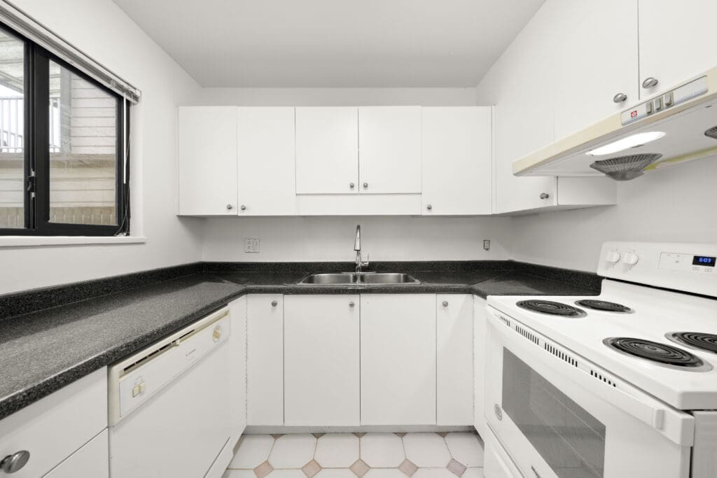 Modern kitchen with white cabinets, black countertops, white electric stove, dishwasher, stainless steel sink, and a window above the countertop.