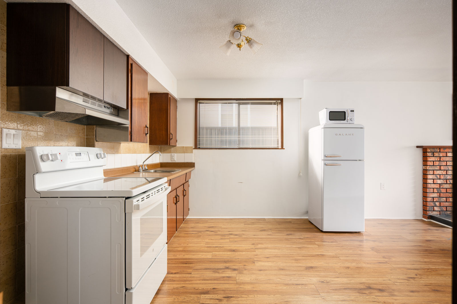 A kitchen with wooden cabinets, a white electric stove, a range hood, a refrigerator with a microwave on top, and wood laminate flooring.