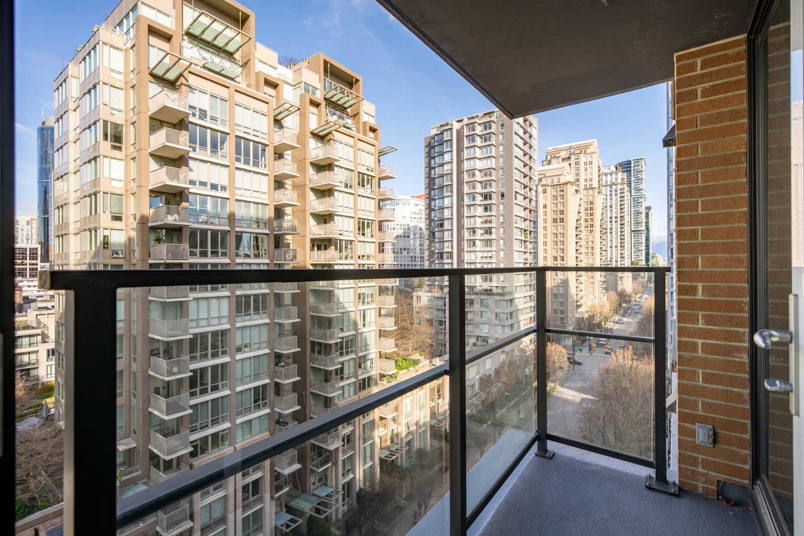 View from a high-rise balcony overlooking a city street surrounded by modern apartment buildings under a clear sky.