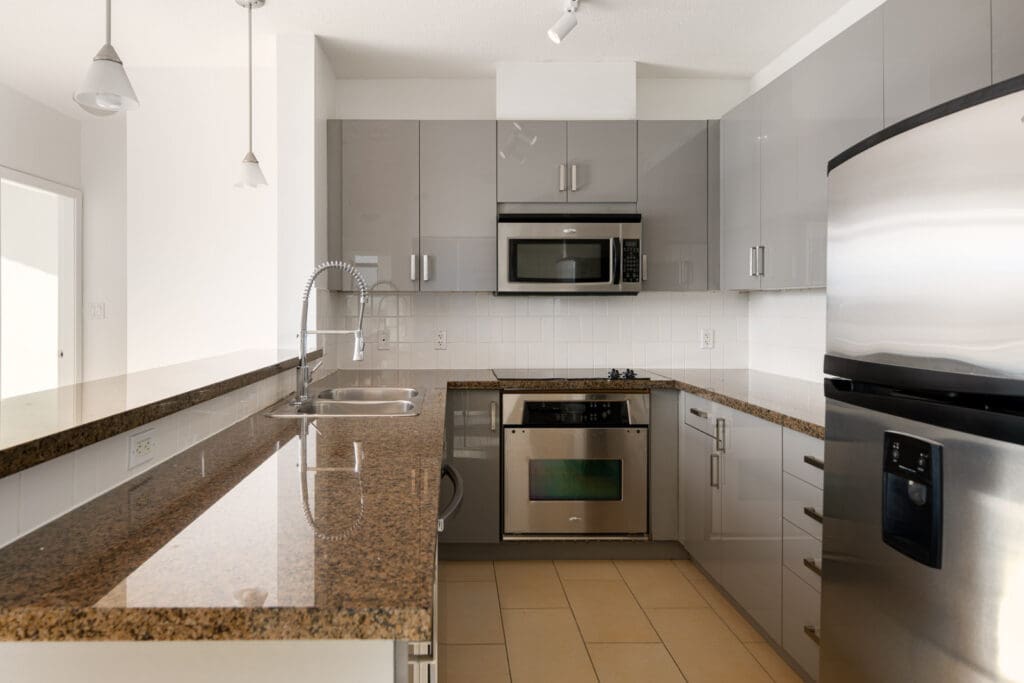 Modern kitchen with granite countertops, stainless steel appliances, grey cabinets, double sink, and tile floor under bright, natural lighting.