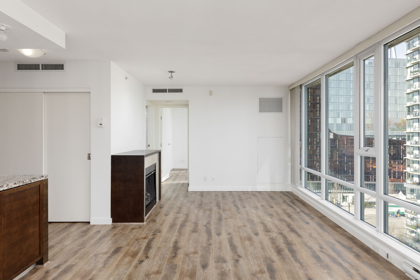 Unfurnished modern apartment with large windows, wood flooring, white walls, a fireplace, and a view of nearby buildings.