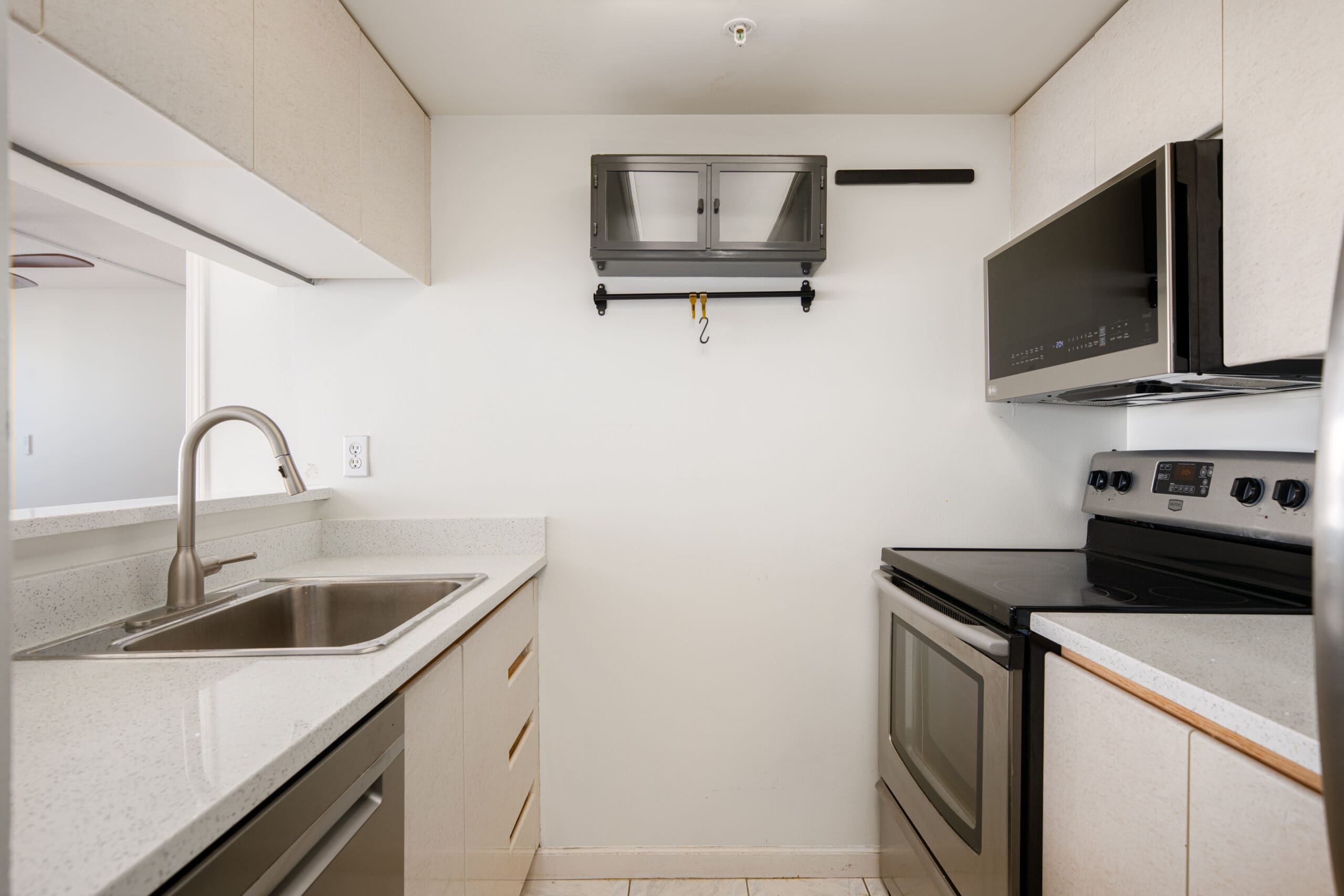 Small modern kitchen with light-colored cabinets, stainless steel sink, electric stove, microwave, and a wall-mounted glass cabinet above the counter.