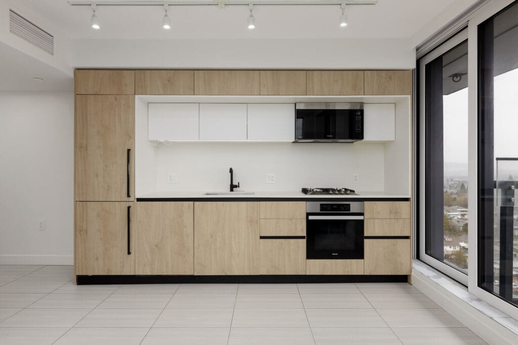 Modern kitchen with light wood cabinetry, black fixtures, built-in oven, microwave, and large windows providing natural light.