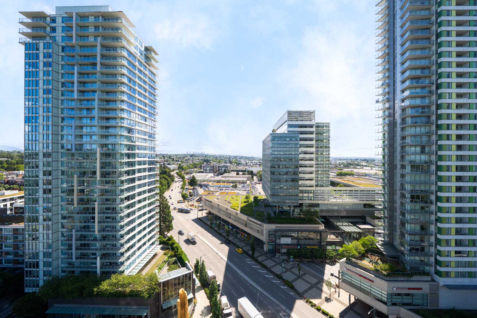 A cityscape view of modern high-rise buildings and a busy intersection with cars and pedestrians on a sunny day.
