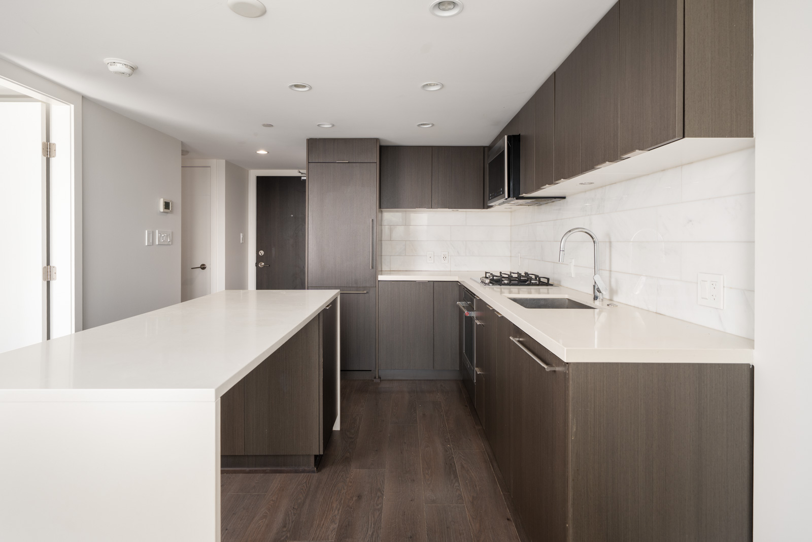 Modern kitchen with dark wood cabinets, white countertops, built-in appliances, gas stove, and a long island; bright, minimal, and uncluttered design.