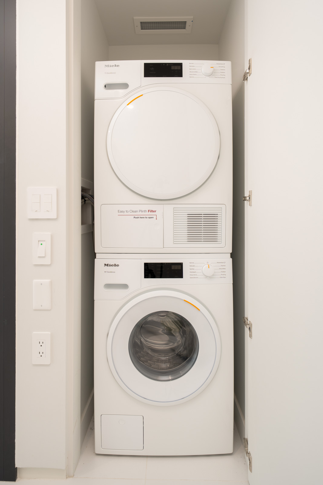 A stacked washer and dryer set installed in a small laundry closet with white walls and door.