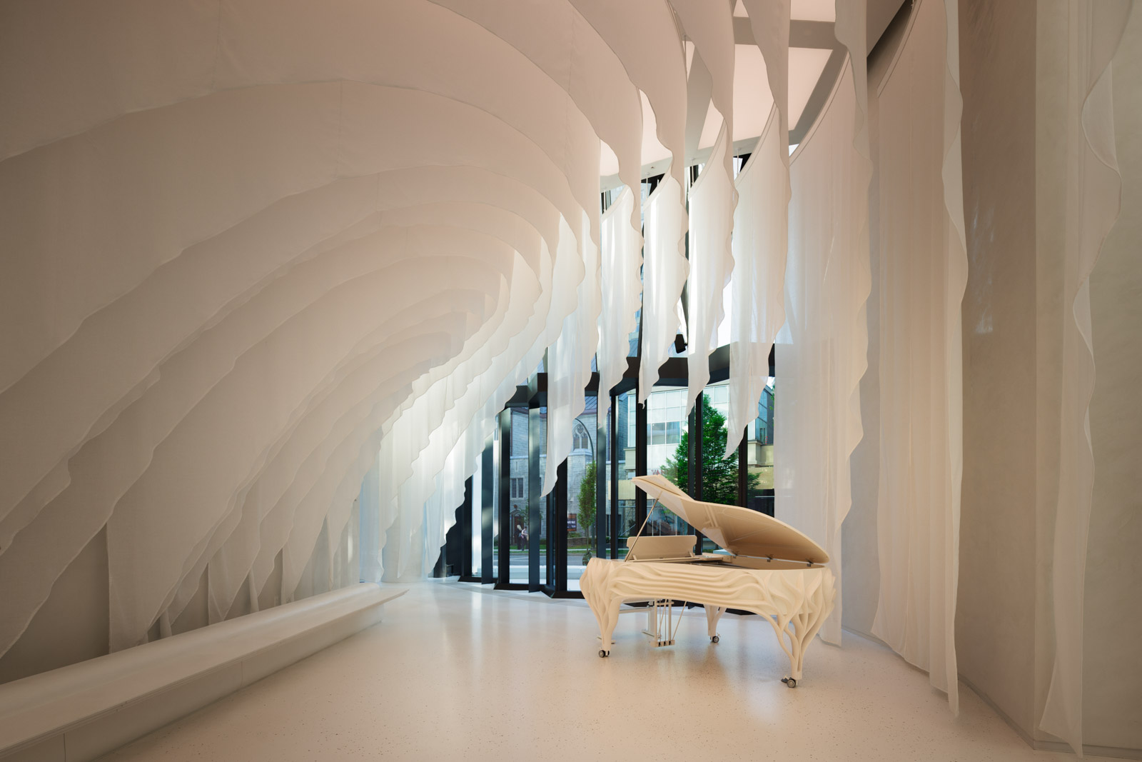 A modern room with layered white fabric panels, a white grand piano, floor-to-ceiling windows, and minimalistic decor.
