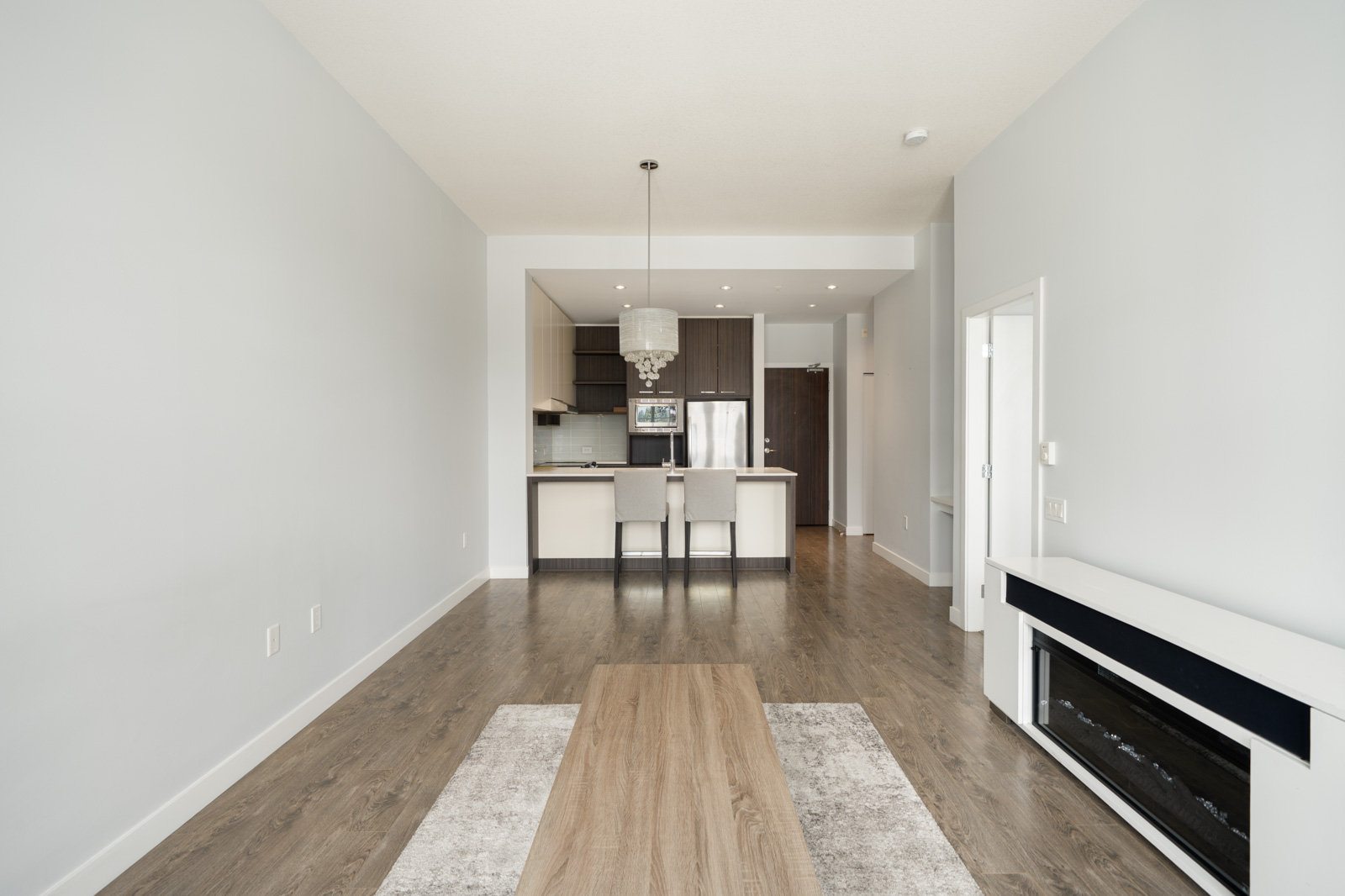 Modern, unfurnished open-concept living space with hardwood floors, a kitchen island with stools, pendant lighting, and a built-in fireplace on the right wall.
