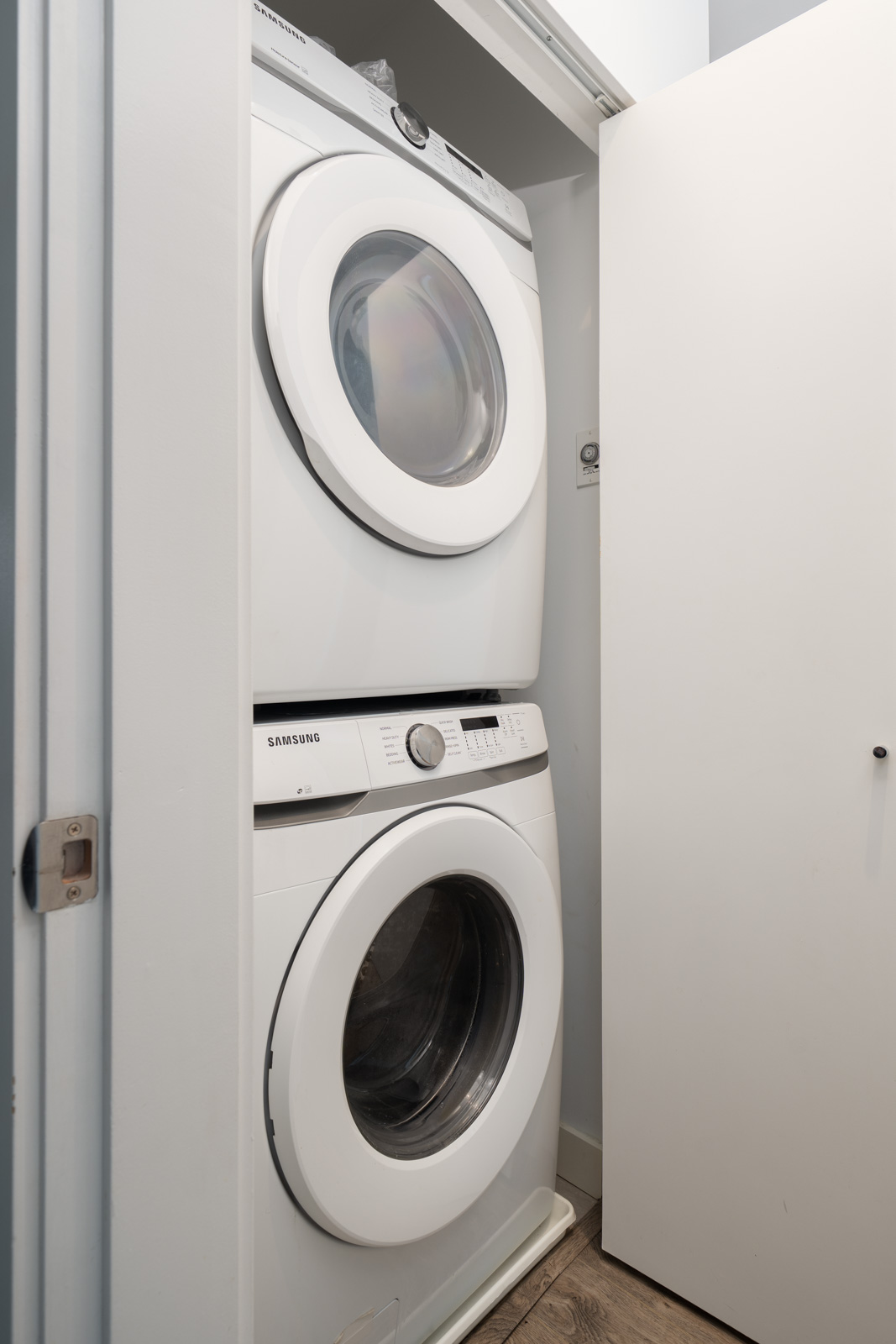 A stacked washer and dryer set is placed inside a small laundry closet with the door partially open.