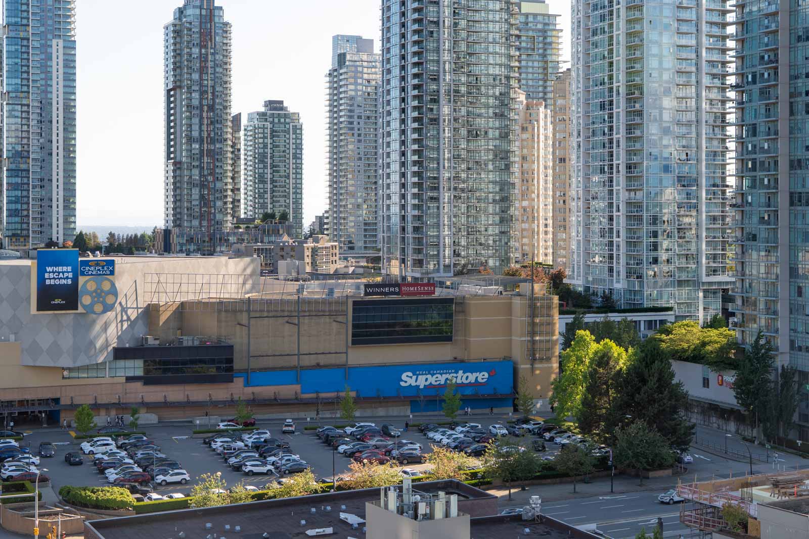 A Superstore with a parking lot in front is surrounded by tall modern apartment buildings in a cityscape.