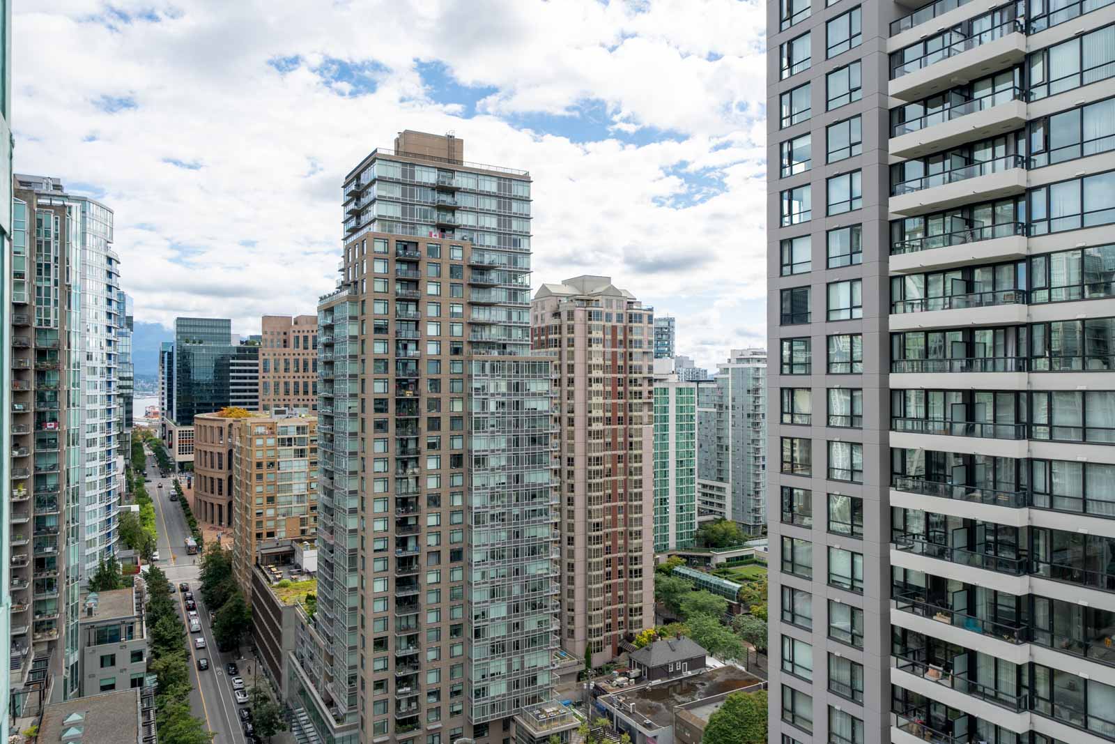 High-rise apartment and office buildings line a city street, with cars visible below and a partly cloudy sky above.